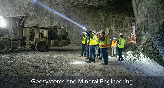 Group wearing reflective vests and hardhats in underground mine with flashlights.  