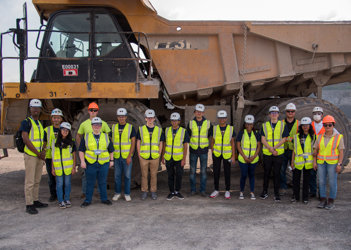 Group of students in safety gear standing in front of a gigantic yellow dump truck.