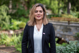  Elham Rahimi in a floral blouse stands in a lush garden with hydrangeas and greenery.